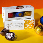 Box of Belgian hot chocolate bombs with colorful wrappers on a yellow and orange background