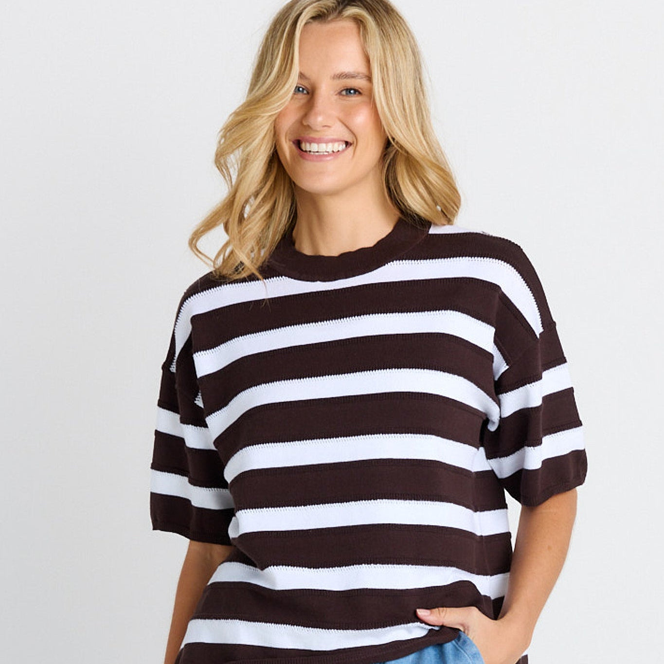 Woman wearing a black and white striped sweater and blue jeans on a plain background