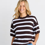 Woman wearing a black and white striped sweater and blue jeans on a plain background