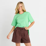 A woman modeling a green and white striped short-sleeve t-shirt and brown linen drawstring shorts against a light gray studio background.
