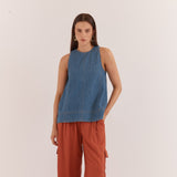 A woman stands against a plain off-white studio background wearing a sleeveless blue denim top and rust-orange wide-leg pants with side cargo pockets.