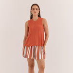 Woman wearing a sleeveless orange top and striped shorts on a white background
